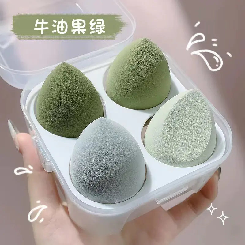 Set of green and gray makeup sponges in a white case held by a hand.