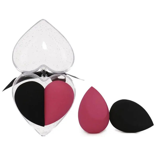 Heart-shaped makeup sponge with black and pink sections next to a clear heart-shaped case on a white background.
