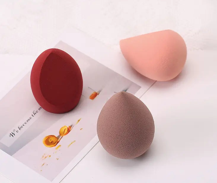 Three makeup sponges on a white surface with a magazine underneath.