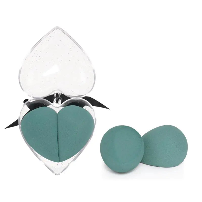 Teal heart-shaped makeup sponges with a clear heart-shaped display case on a white background