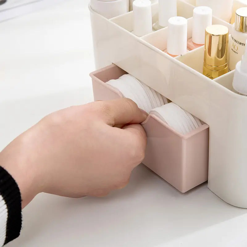 Hand reaching into a pink cosmetic organizer filled with makeup items on a white surface.