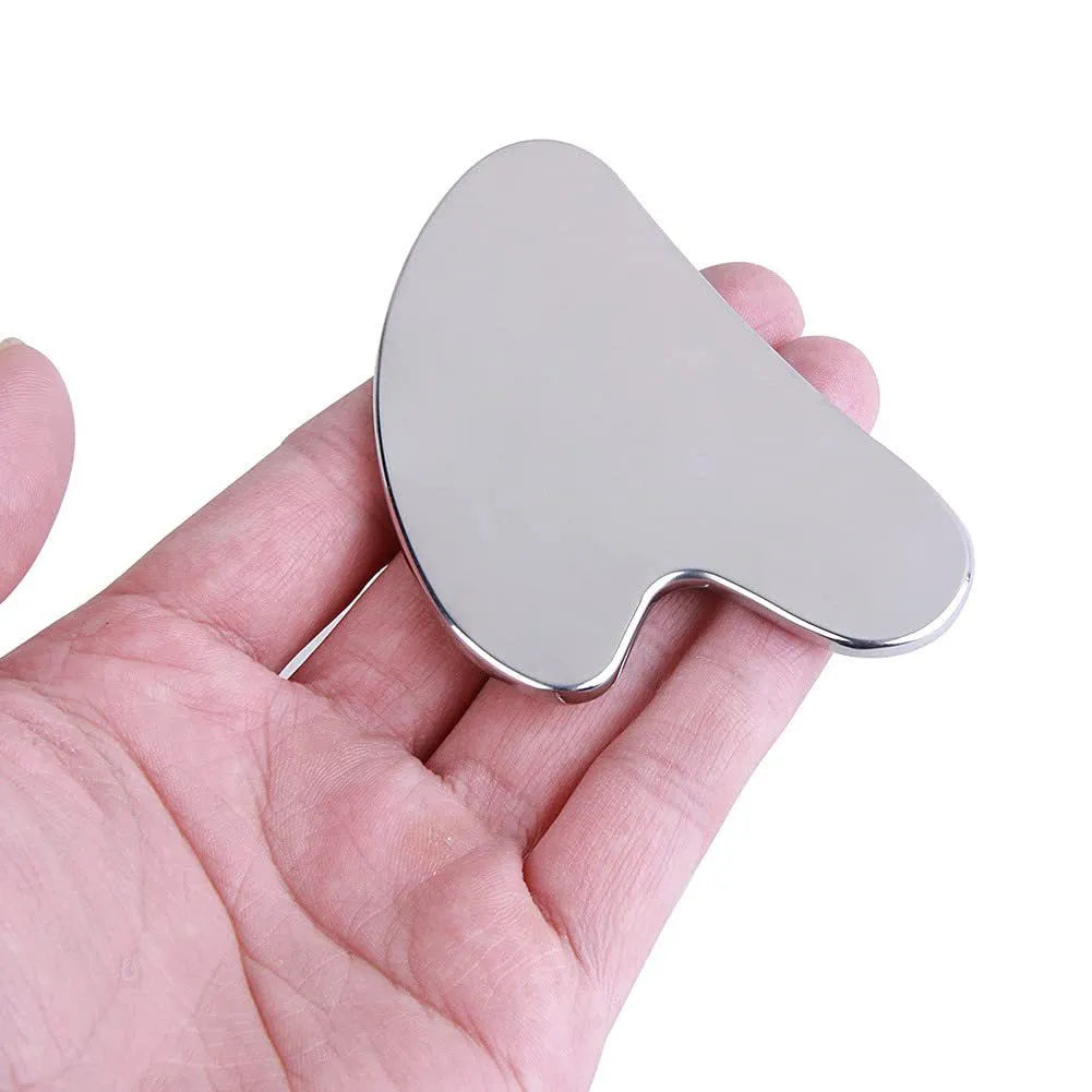 Heart-shaped silver gua sha tool held in a hand against a white background