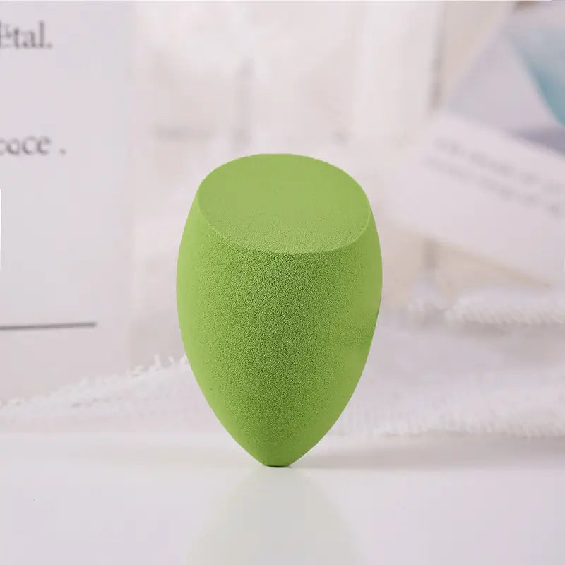 Green makeup sponge on a white surface with a blurred background