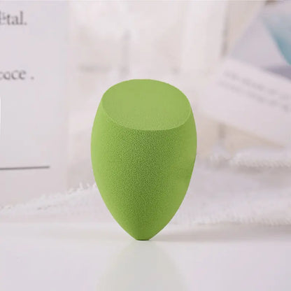Green makeup sponge on a white surface with a blurred background