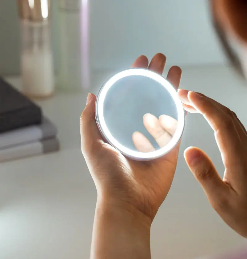 Person holding a round compact mirror with a light on a blurred background