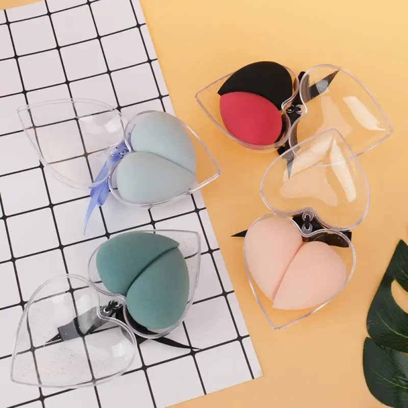 Set of makeup sponges in clear cases on a grid and yellow surface with a leaf.