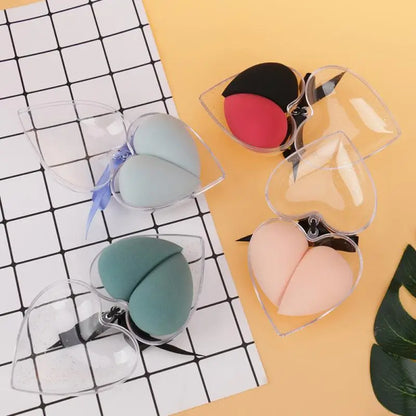 Set of makeup sponges in clear cases on a grid and yellow surface with a leaf.