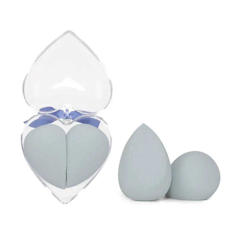 Two gray makeup sponges with a clear heart-shaped container on a white background