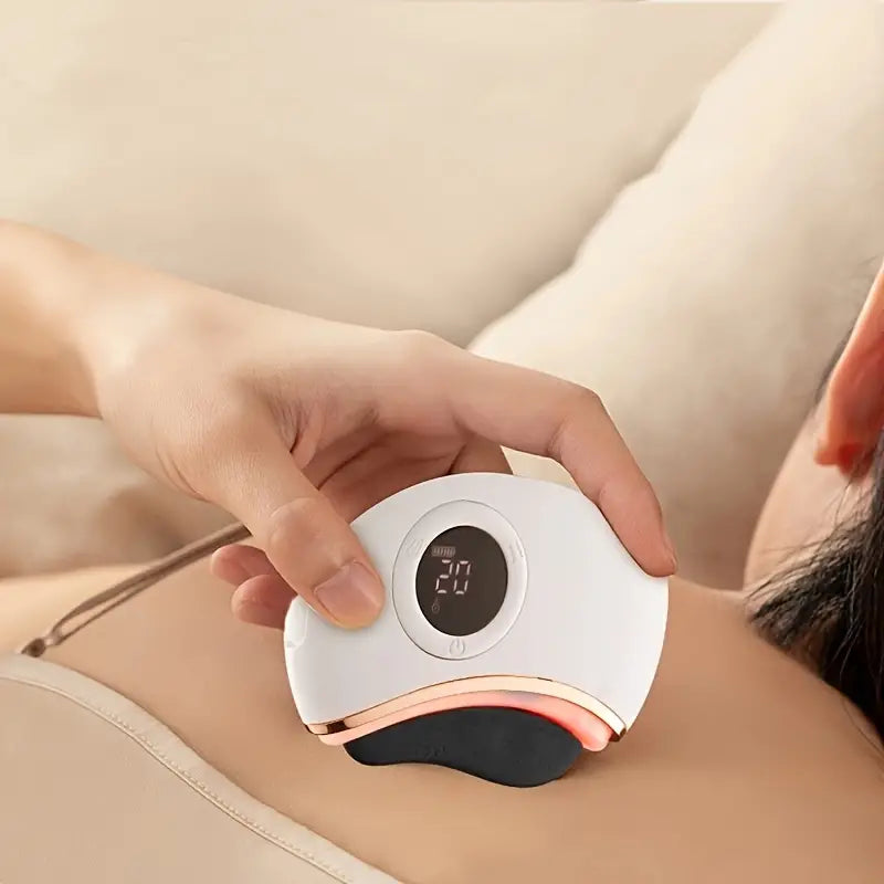 Person using a handheld electronic gua sha device on their shoulder with a blurred background