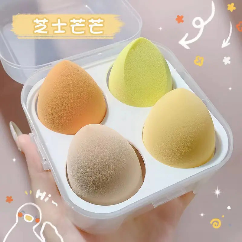 Four makeup sponges in a clear container held by a hand with decorative elements.