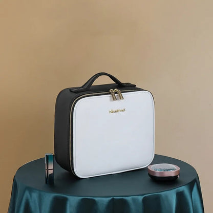 White and black cosmetic bag with gold lock on a green surface against a beige background
