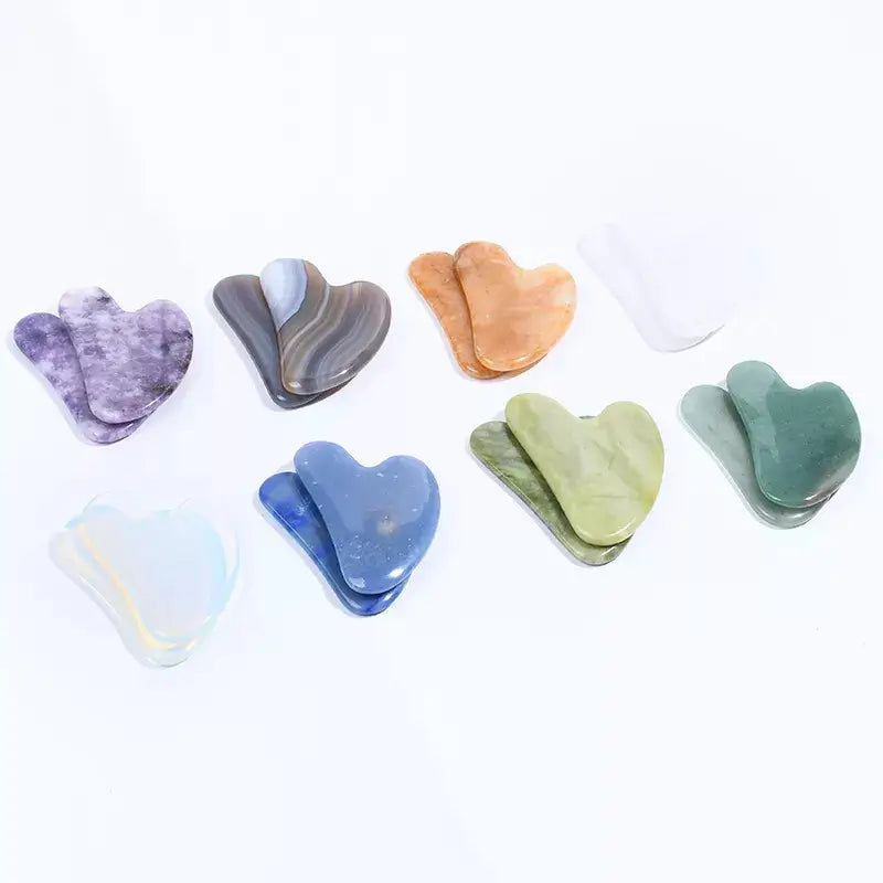 Set of heart-shaped gua sha tools in various colors on a white background