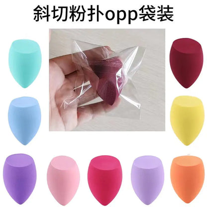 Colorful makeup sponges with a clear bag containing pink sponge, on a light gray background.