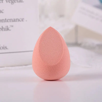 Pink makeup sponge on a light surface with blurred text in the background