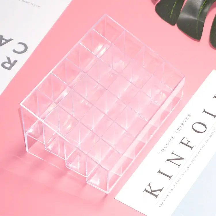 Clear acrylic cosmetic organizer on a pink surface with a magazine underneath