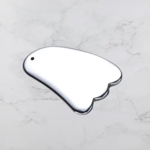 Gua sha tool shaped like a cloud on a marble surface