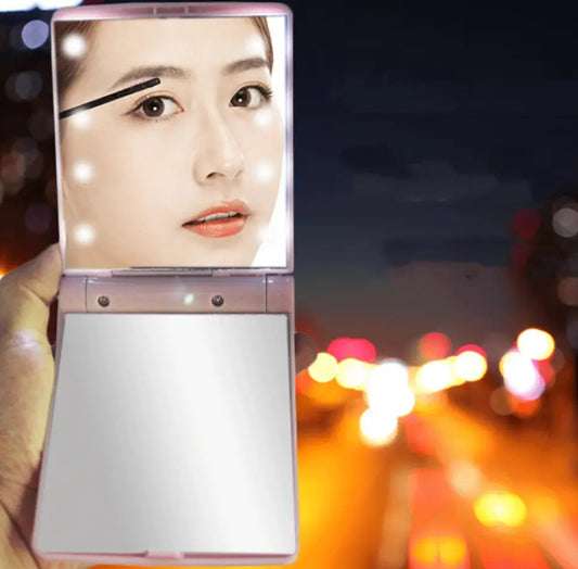Foldable makeup mirror held by a person with blurred city lights in the background