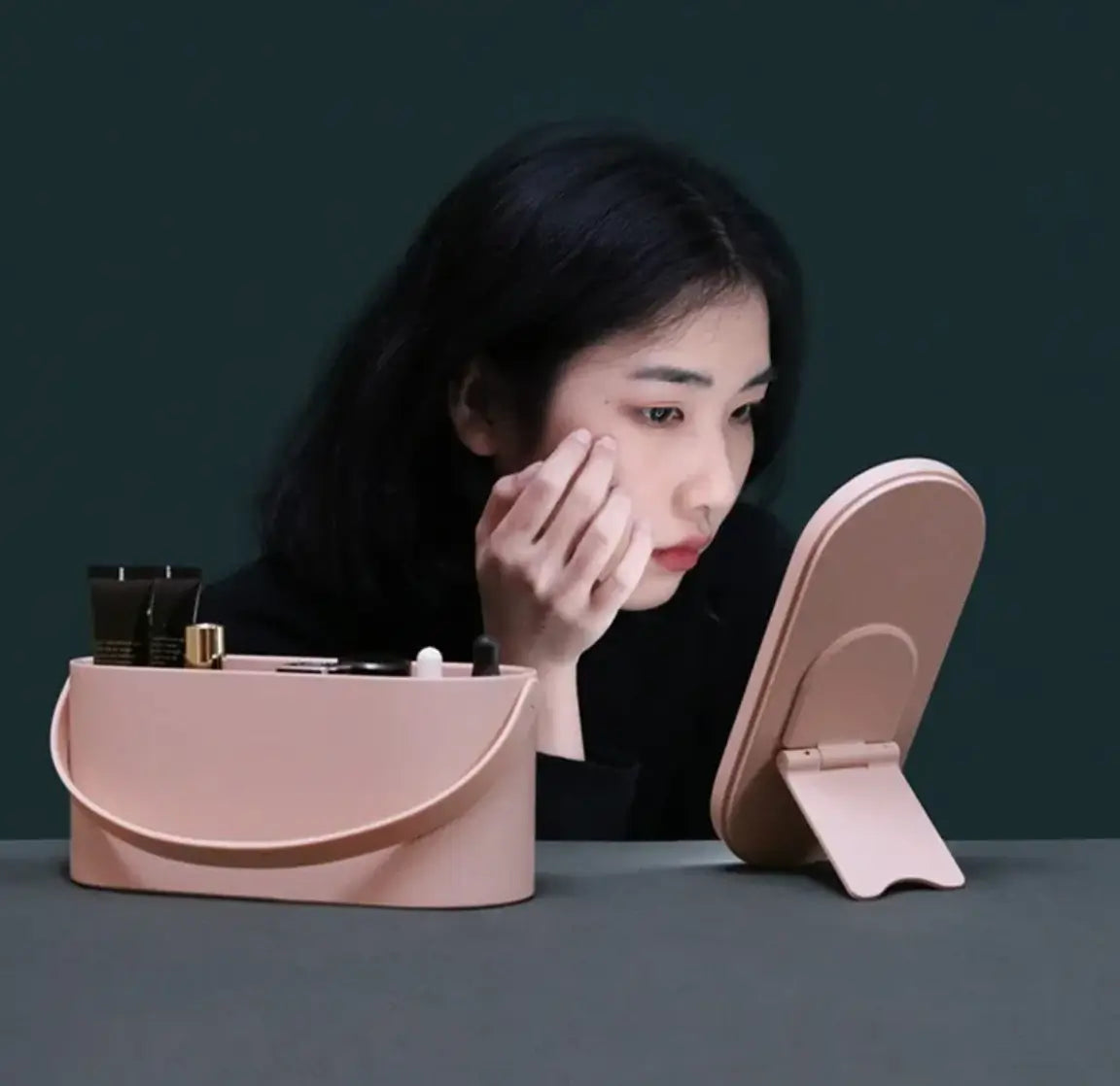 Woman applying makeup in front of a pink mirror and cosmetic bag on a dark background