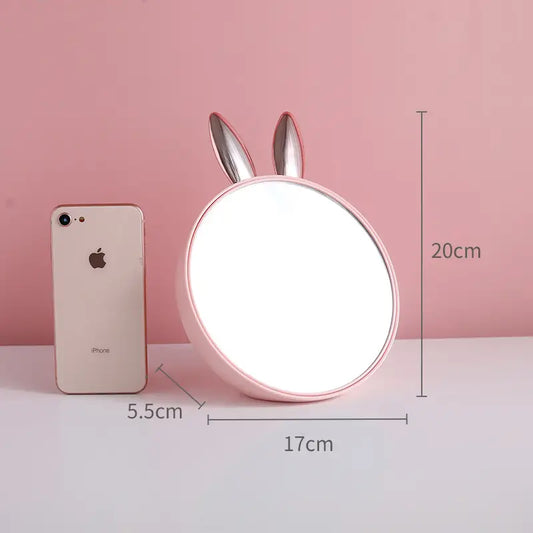 Round mirror with bunny ears next to a smartphone on a pink background